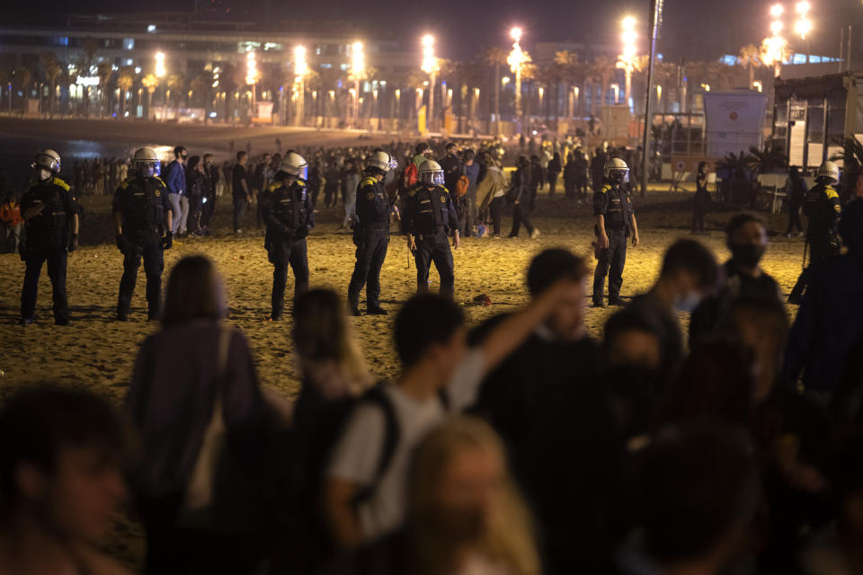 Police officers stand guard as people crowded on the beach in Barcelona, Spain, Sunday, May 9, 2021. Barcelona residents were euphoric as the clock stroke midnight, ending a six-month-long national state of emergency and consequently, the local curfew. Spain is relaxing overall measures to contain the coronavirus this weekend, allowing residents to travel across regions, but some regional chiefs are complaining that a patchwork of approaches will replace the six-month-long national state of emergency that ends at midnight on Saturday. (AP Photo/Emilio Morenatti)