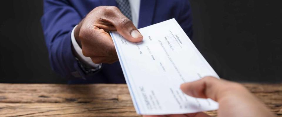 Close-up Of A Businessman's Hand Giving Cheque To Colleague Over Wooden Desk