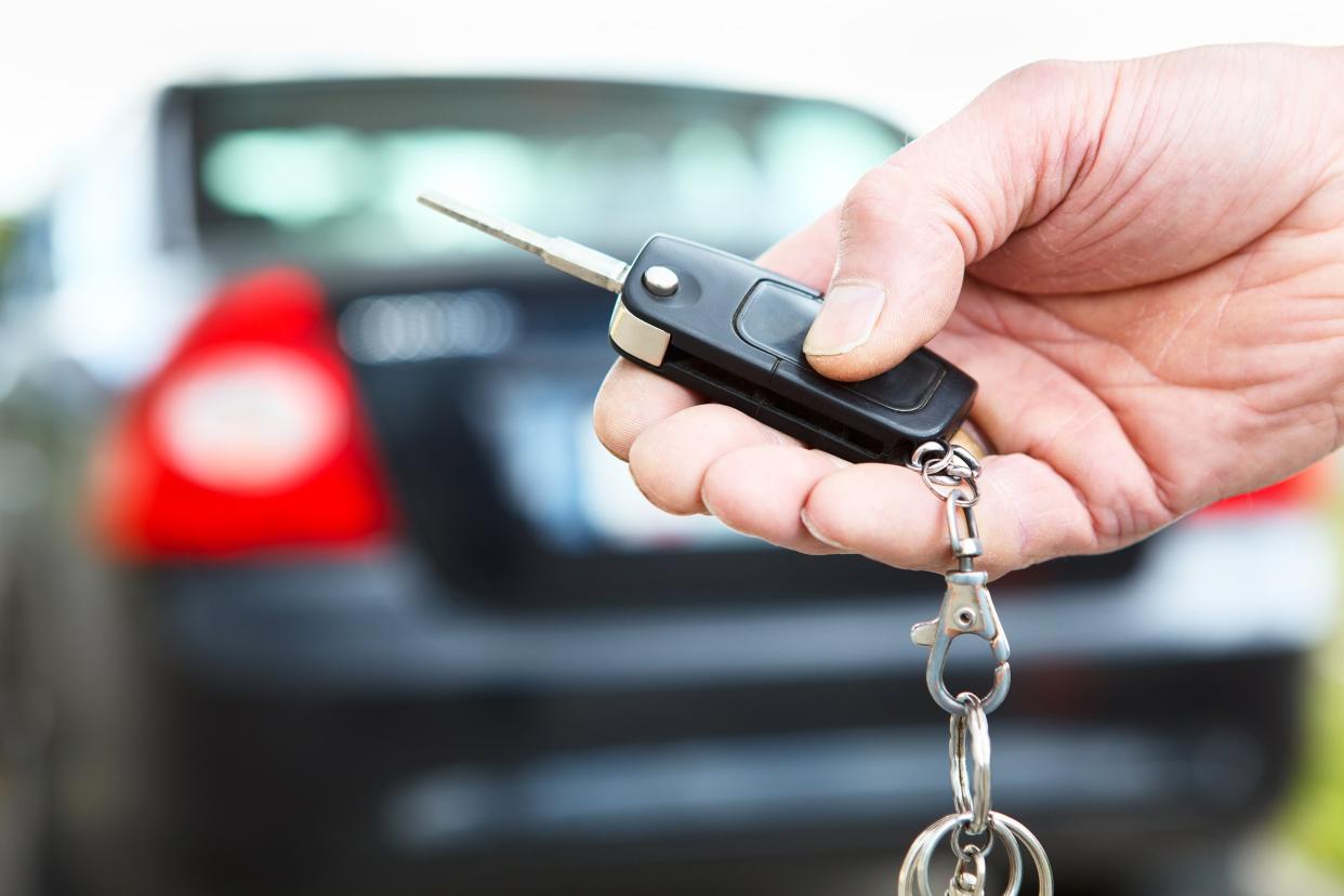 men's hand presses on the car key and remote in front of rental car