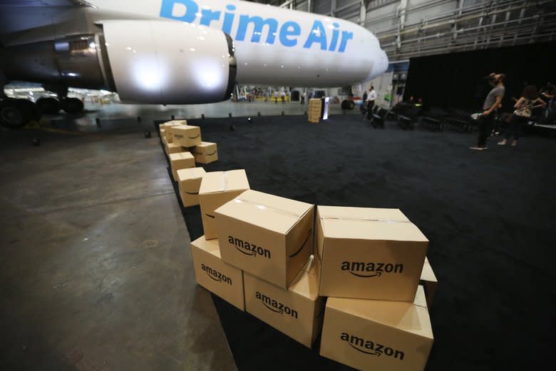 Amazon boxes sitting in an airport hangar in front of a Prime Air cargo plane.