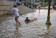 One woman pulls another on a body board through water on the quad of UCLA after flooding from a broken 30-inch water main under nearby Sunset Boulevard inundated a large area of the campus in the Westwood section of Los Angeles, Tuesday, July 29, 2014. The 30-inch (75-centimeter) 93-year-old pipe that broke made a raging river of the street and sent millions of gallons (liters) of water across the school's athletic facilities, including the famed floor of Pauley Pavilion, the neighboring Wooden Center and the Los Angeles Tennis Center, and a pair of parking structures that took the brunt of the damage. (AP Photo/Mike Meadows)