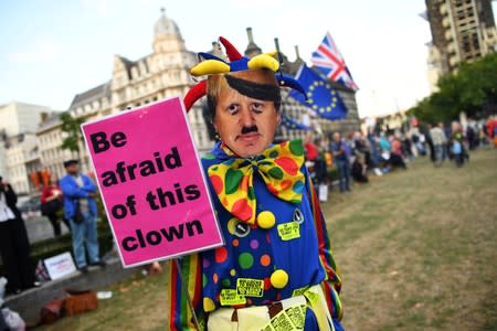 An anti-Brexit protester wearing a clown costume and a defaced mask depicting British Prime Minister Boris Johnson holds a placard outside the Houses of Parliament in London