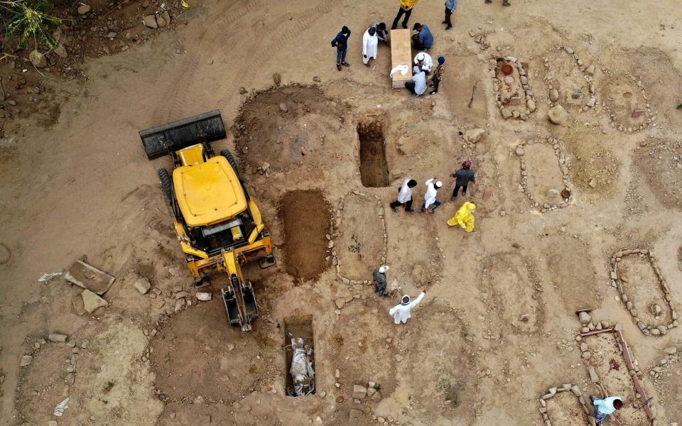 Relatives and friends gather to bury the dead bodies of Covid-19 victims at a graveyard in New Delhi - AFP