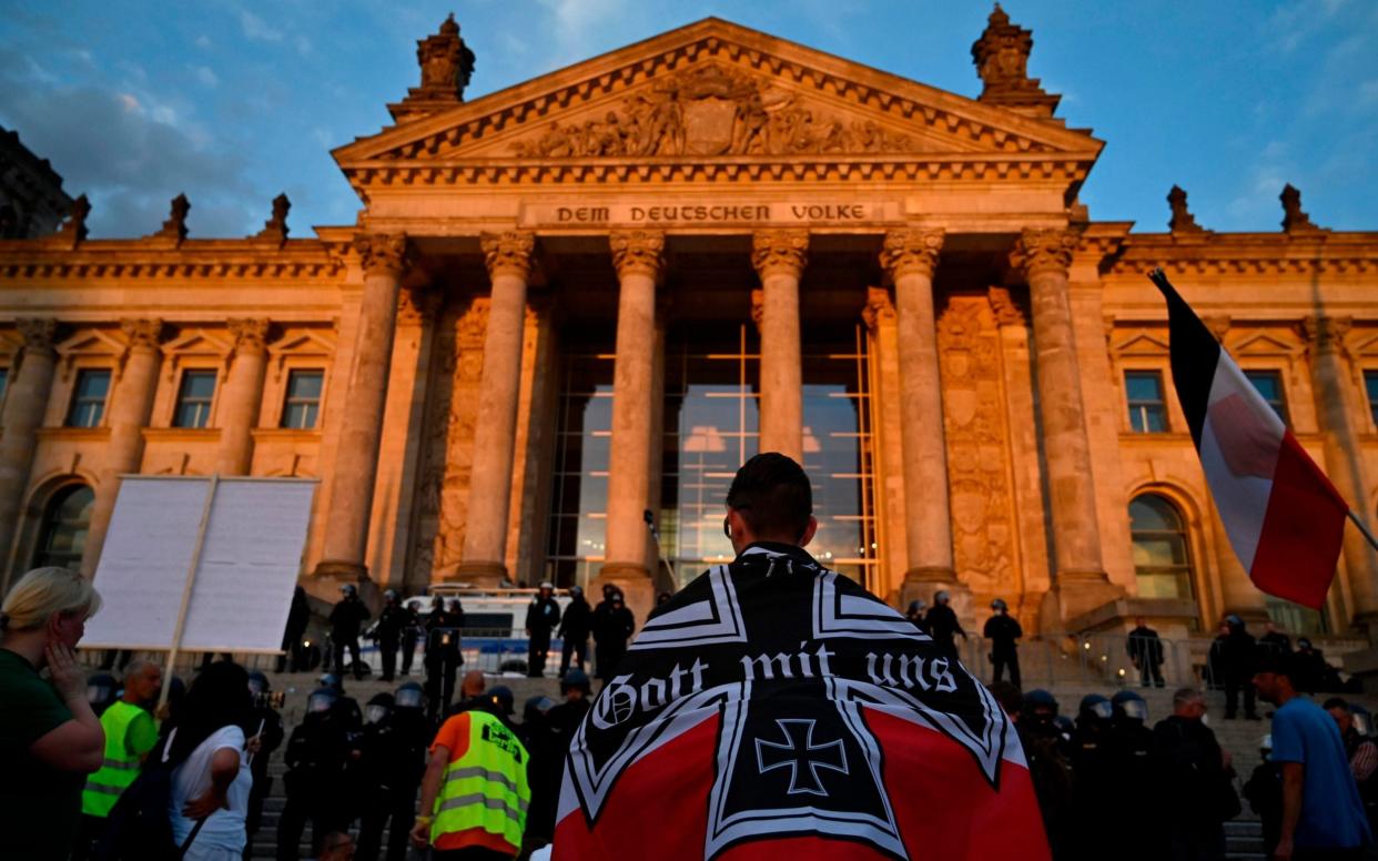 A protester stands wrapped in black-white-red imperial German flag in front of the Reichstag building - AFP