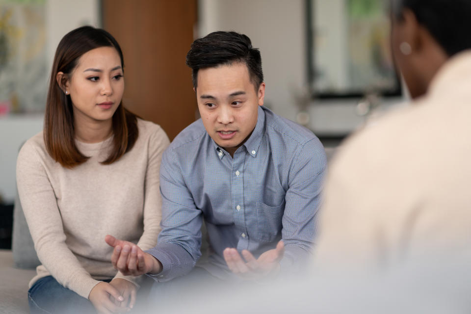 An Asian married couple talks to a therapist together about their life. They are attentive and focused on making their marriage work.