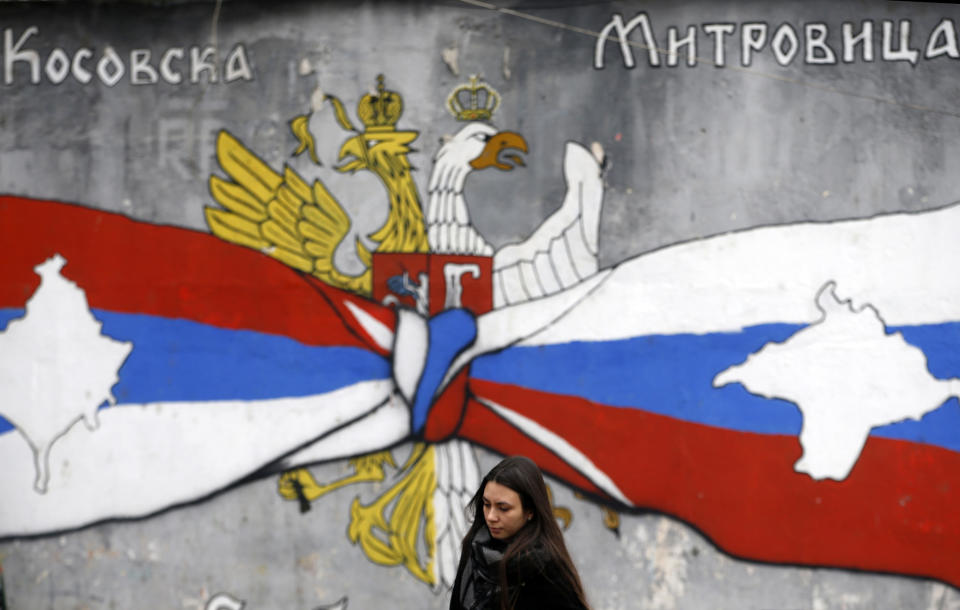 A woman walks by graffiti showing the Serbian flag, left, and Russian flags with maps of Kosovo and Crimea in northern, Serb-dominated part of ethnically divided town of Mitrovica, Kosovo, Saturday, Dec. 15, 2018. Serbia threatened a possible armed intervention in Kosovo after the Kosovo parliament on Friday overwhelmingly approved the formation of an army. Russia denounced the move to form a Kosovo army, saying the ethnic Albanian force must be "disbanded" by NATO in Kosovo. (AP Photo/Darko Vojinovic)