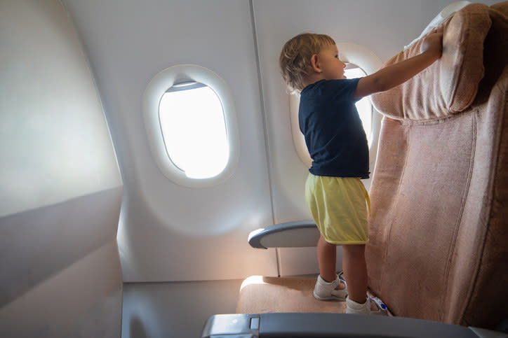 A toddler dangerously stands up on a seat in a plane