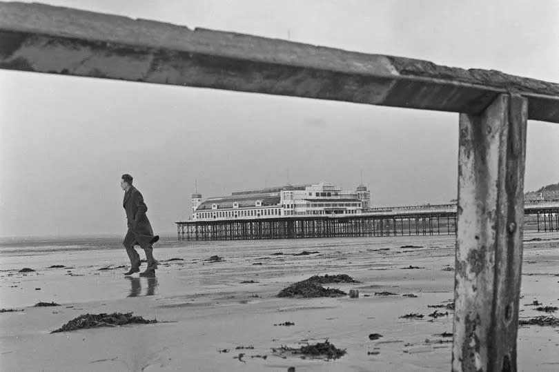 A lone man walks along the beach at Weston-super-Mare with the Grand Pier in the background. 17th November 1959