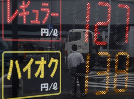 A man and vehicles are reflected in a price display at a gas station in Tokyo August 26, 2015. REUTERS/Toru Hanai