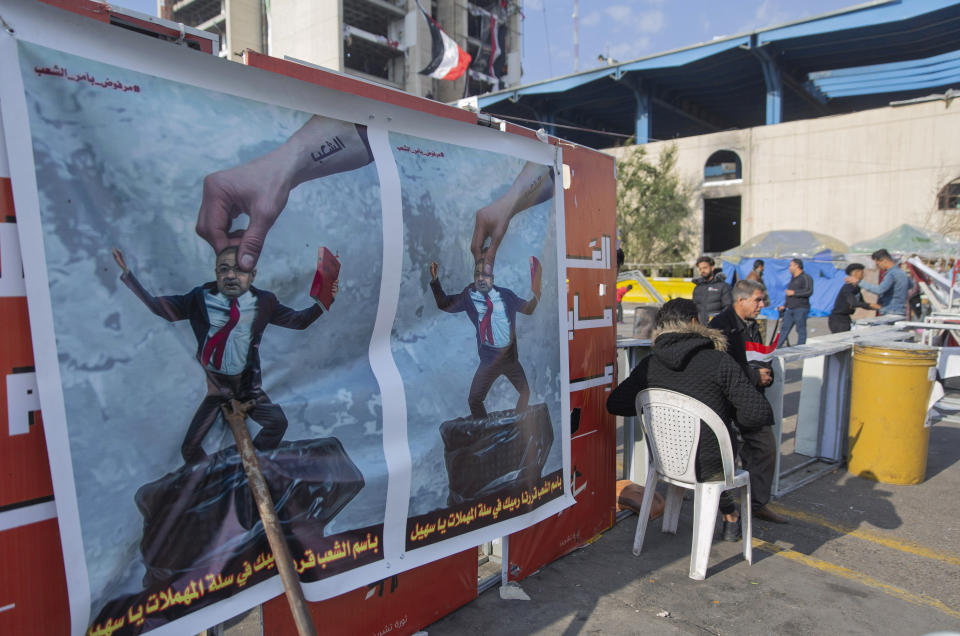 Protesters go through security inspection next to posters that depicts Qusay al-Suhail, a candidate for the prime minister's post, and Arabic that reads, "in the name of the people, you will be dumped in the garbage container Suhail," during ongoing protests, in Tahrir square, in Baghdad, Iraq, Wednesday, Dec. 25, 2019. (AP Photo/Nasser Nasser)