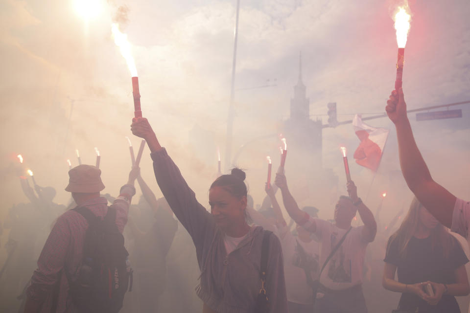 People stand on the city's main intersection holding national flags and flares to observe a minute of silence for the fighters and victims of the 1944 Warsaw Uprising against the Nazi German occupiers, in Warsaw, Poland, Monday Aug. 1, 2022. Poles are marking the 78th anniversary of the Warsaw Uprising, a doomed revolt against Nazi German forces during World War II. (AP Photo/Michal Dyjuk)