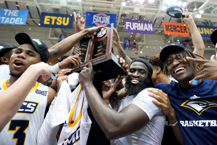 Chattanooga guard David Jean-Baptiste, second from right, holds the championship trophy with teammates to celebrate their win over Furman in an NCAA college basketball championship game for the Southern Conference tournament, Monday, March 7, 2022, in Asheville, N.C. (AP Photo/Kathy Kmonicek)