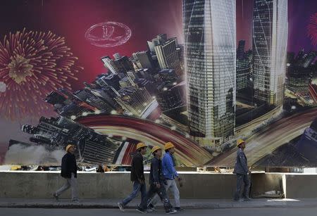 Construction workers walk past an advertisement board in Kunming, Yunnan province, January 25, 2015. REUTERS/Wong Campion