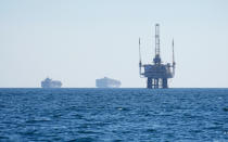 A couple of cargo vessels are seen anchored offshore, sharing space with several oil platforms, before heading into the Los Angeles-Long Beach port, Tuesday, Oct. 5, 2021. (AP Photo/Eugene Garcia)