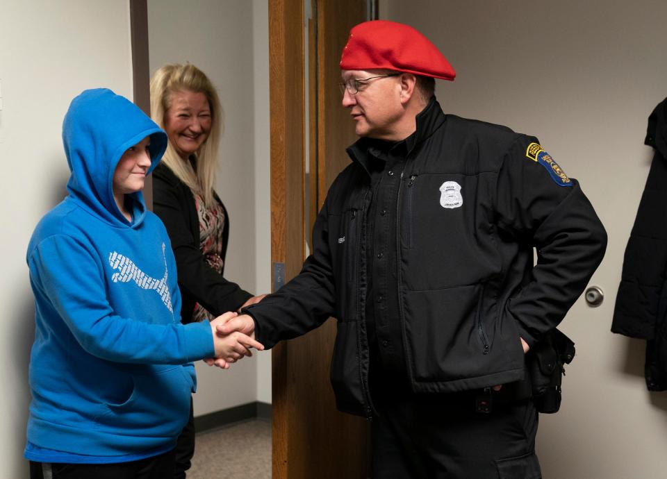 William Denny, 12, a Lincoln Park Middle School seventh grader, left, shakes hands with Lincoln Park Police Reserve officer Matt Werling as his principal Tara Randall stands behind him.Denny was singled out for being an exceptional student and gifted $100 by a Secret Santa elf in Lincoln Park Monday, Dec. 5, 2022.