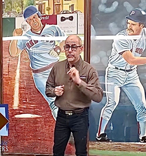 Auctioneer Kevin Bruneau stands in front of framed murals of former Red Sox players Marty Barrett, left, and Wade Boggs.