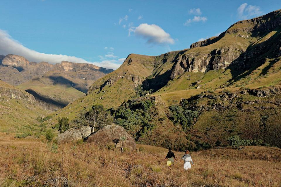 Two people walking through grassland in a national park surrounded by grass mountains