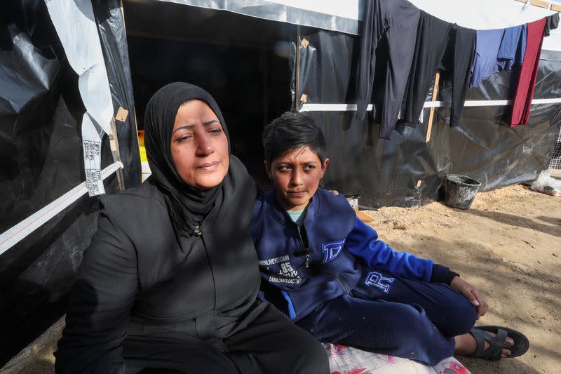 Ahmed Jarbou, a displaced Palestinian boy whose father was killed in an Israeli strike, sits next to his mother outside their makeshift shelter, in Rafah in the southern Gaza Strip