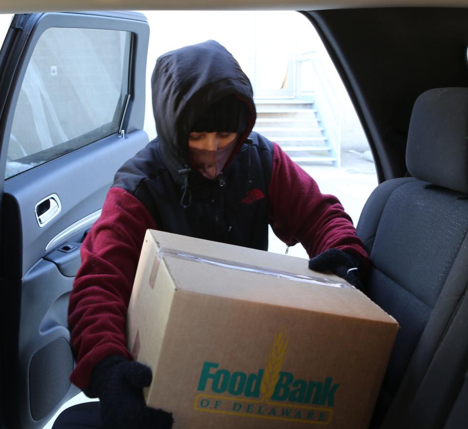 Adrianna Tutini, a driver for Amazon Flex, loads a box of food from the Food Bank of Delaware into the back seat of her SUV.