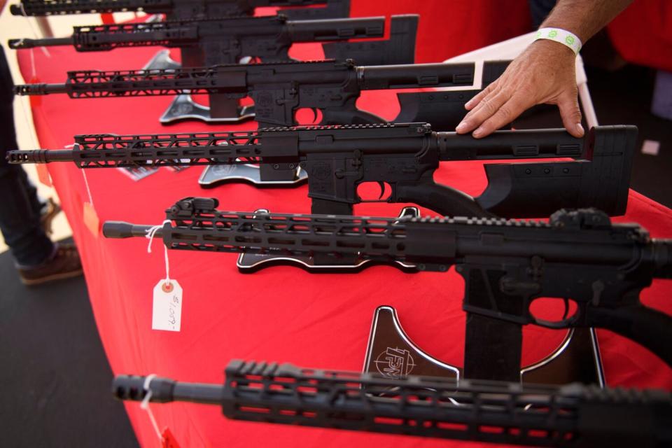 Laid out on a red cloth a row of AR-15 style rifles are displayed for sale at a gun show