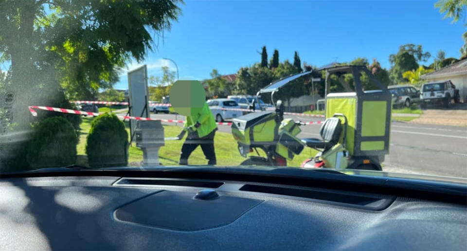 An Australian Post worker delivering letters to a house with a bike parked near the letterbox.