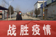 A man wearing a face mask stands near a banner reading "defeat the epidemic" stretched across the entrance to Donggouhe village in northern China's Hebei Province, Wednesday, Jan. 29, 2020. With barricades and wary guardians, villages on the outskirts of Beijing are closing themselves off to outsiders to ward against infection amid the outbreak of a new type of virus. (AP Photo)