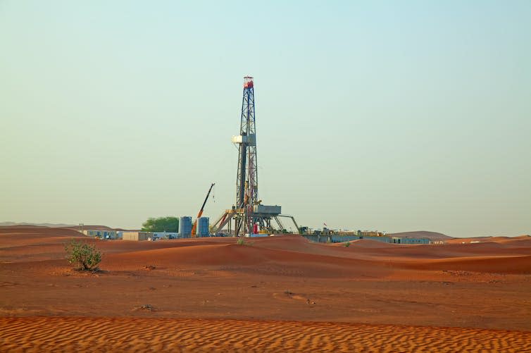 An oil drilling platform rising above red desert sand.