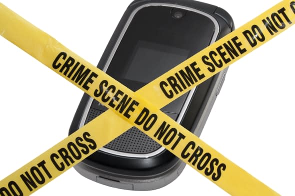A mobile cell phone is blocked by yellow police tape reading Crime Scene Do Not Cross. The concept represents compromised techno