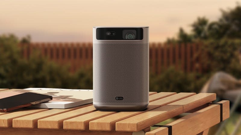 The XGIMI MoGo 2 Pro portable projector sitting on a wooden table in a backyard at dusk.