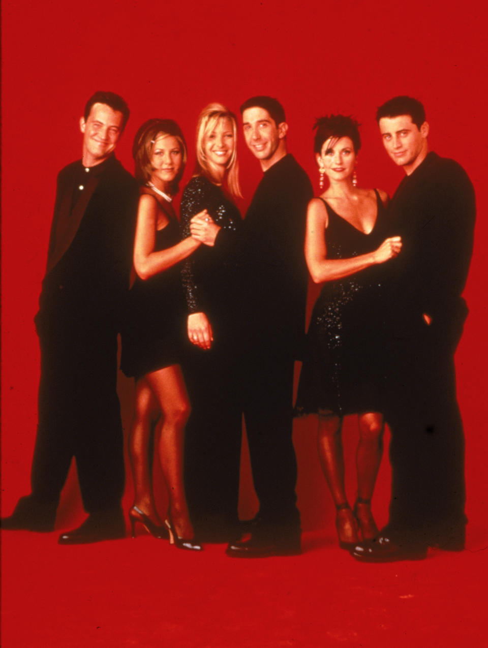 Promotional portait of the cast of the television series, 'Friends,' wearing black against a red backdrop, circa 1995. L-R: Matthew Perry, Jennifer Aniston, Lisa Kudrow, David Schwimmer, Courteney Cox, and Matt LeBlanc. (Photo by Warner Brothers Television/Fotos International/Courtesy of Getty Images) 