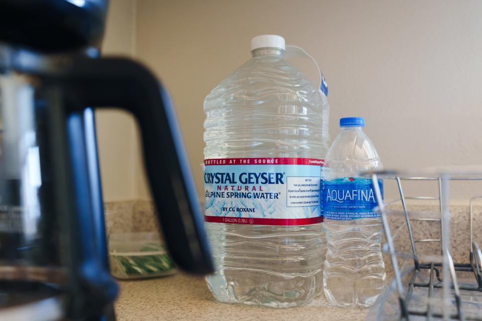 Bottled water sits on a counter near a coffee pot.