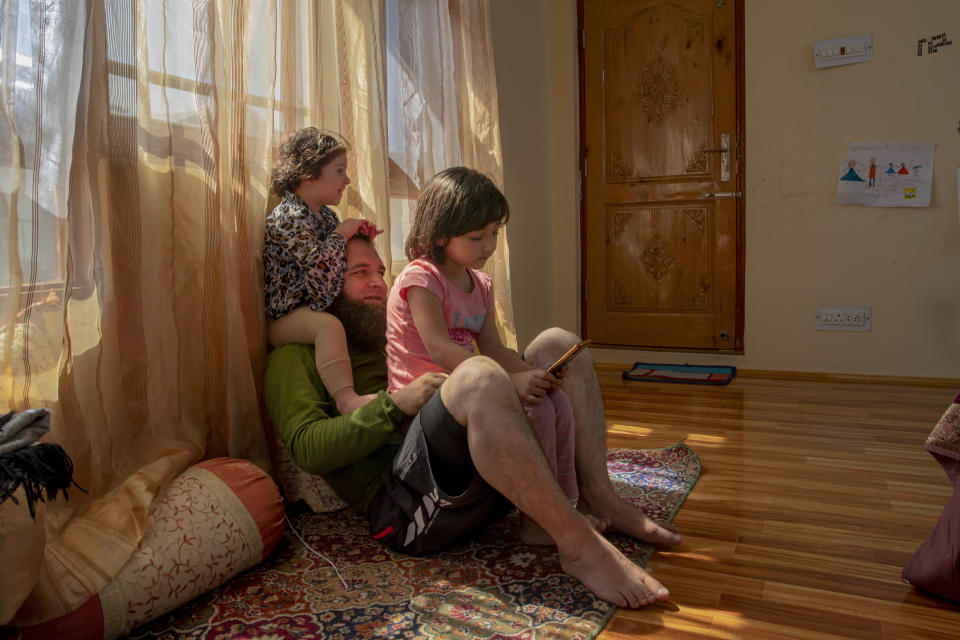 Khalid Bazaz plays with his niece Sundas Irfan, as his daughter Maria Khalid sits on his lap and watches online classes, at their home in Srinagar, Indian controlled Kashmir, Thursday, July 23, 2020. Confined to their homes, students have found it challenging to study online with the painstakingly slow internet connections, which also faces outages following the frequent gunbattles between rebels and Indian soldiers. With no high-speed internet, many educators are unable to upload video lectures and conduct online classes. But some are making the best of limited resources. "I have to spend 3 hours every day with Maria as she is too young to handle zoom meetings and like every child she is not interested in these online classes," Khalid said. (AP Photo/Dar Yasin)