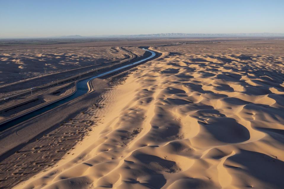 A water canal cuts through sand dunes.