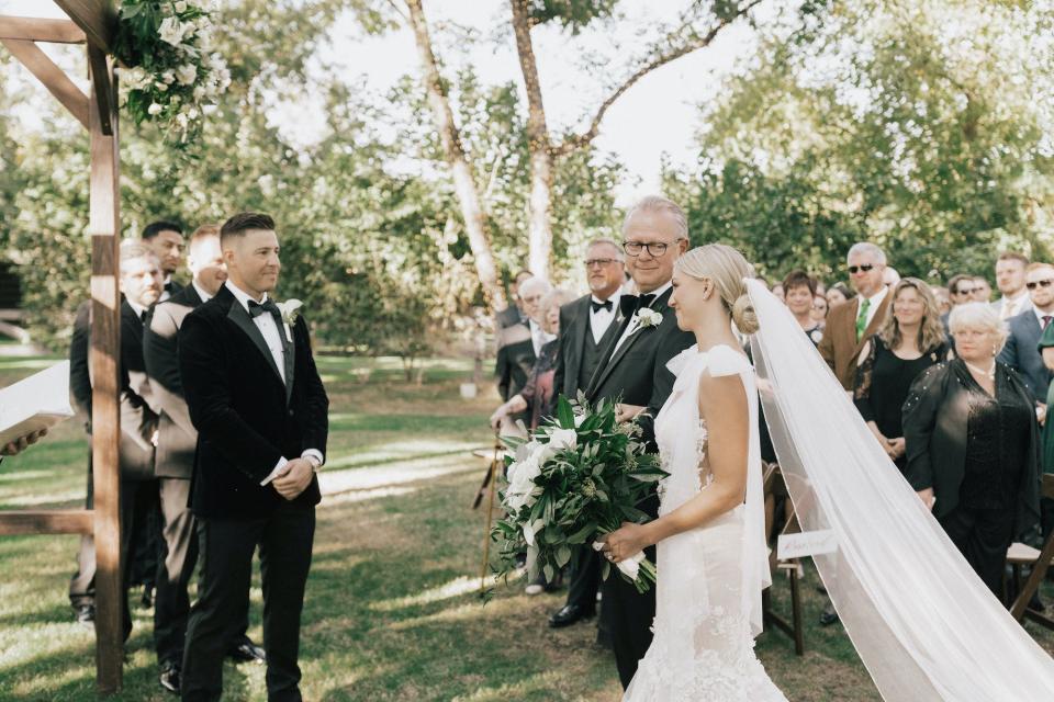 A bride and her father walk towards her groom during their outdoor wedding.