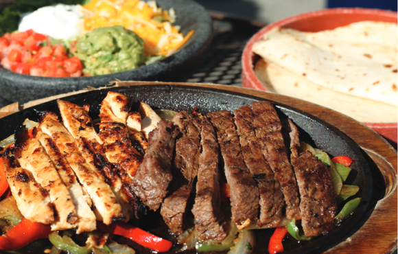 Beef and chicken fajitas with tortillas, cheese, guacamole, salsa, and sour cream.