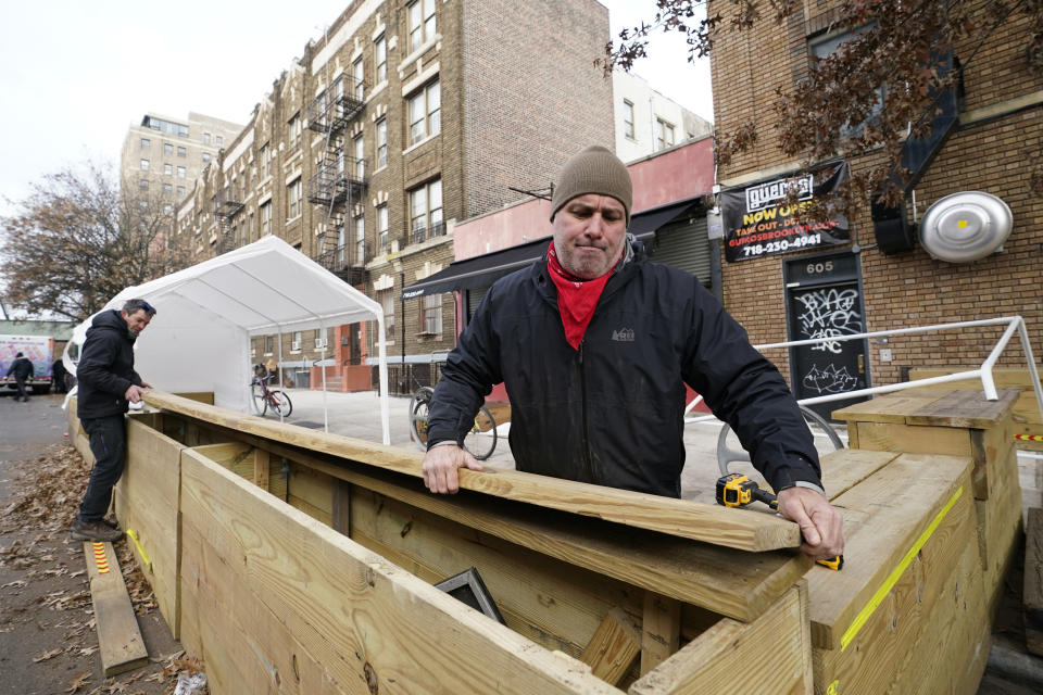 Wade Hagenbart, right, lifts the top off a wooden support barrier for a tent he's constructing for outdoor dining Guero's, the tiny but popular taco and margarita restaurant he co-owns in the Prospect Heights neighborhood of Brooklyn, Wednesday, Dec. 2, 2020, in New York. (AP Photo/Kathy Willens)
