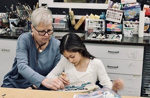 With Hands and Hearts Fiber Artists help members of the Saturday Morning Youth Program with a rug-hooking project.