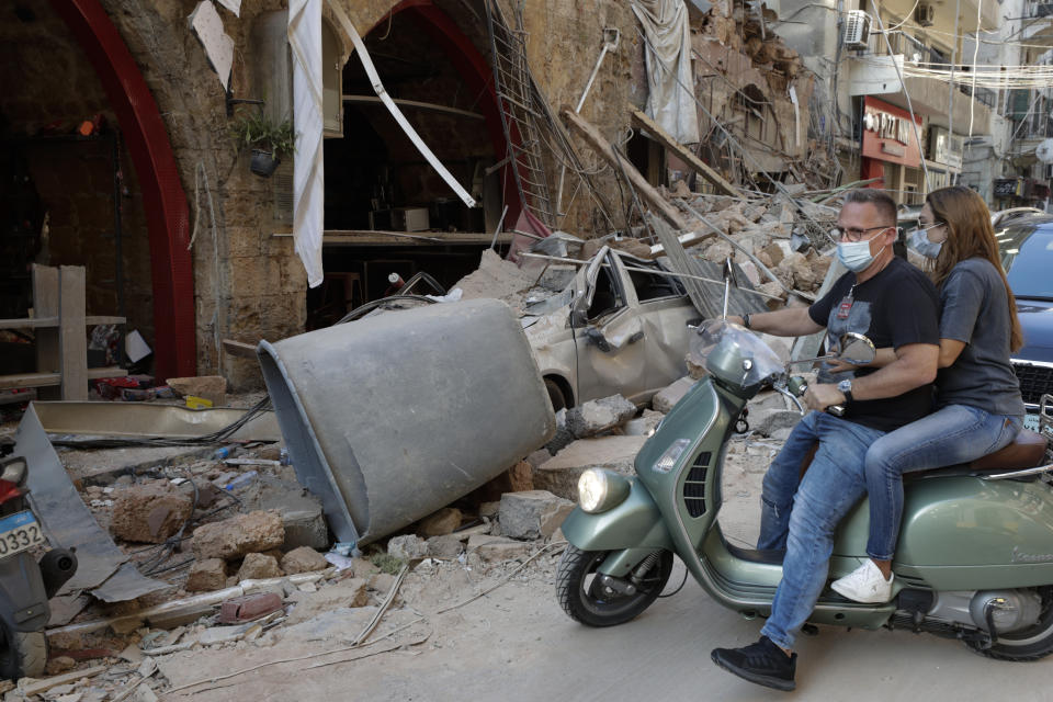 A couple drives past destruction after a massive explosion in Beirut, Lebanon, Wednesday, Aug. 5, 2020. The explosion flattened much of a port and damaged buildings across Beirut, sending a giant mushroom cloud into the sky. In addition to those who died, more than 3,000 other people were injured, with bodies buried in the rubble, officials said.(AP Photo/Hassan Ammar)