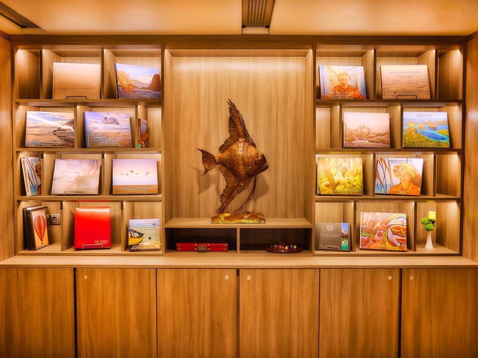 A wooden bookshelf with a large statue of a fish inside The World