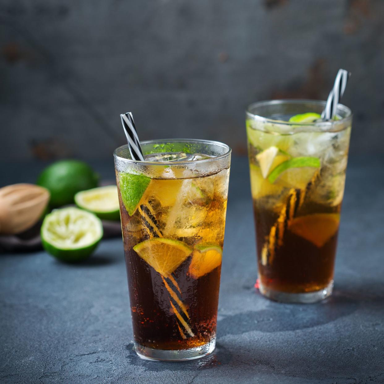 Food and drink, holidays party concept. Cuba libre or long island iced tea alcohol cocktail drink beverage, longdrink in a glass with straw, ice and lime on a dark table