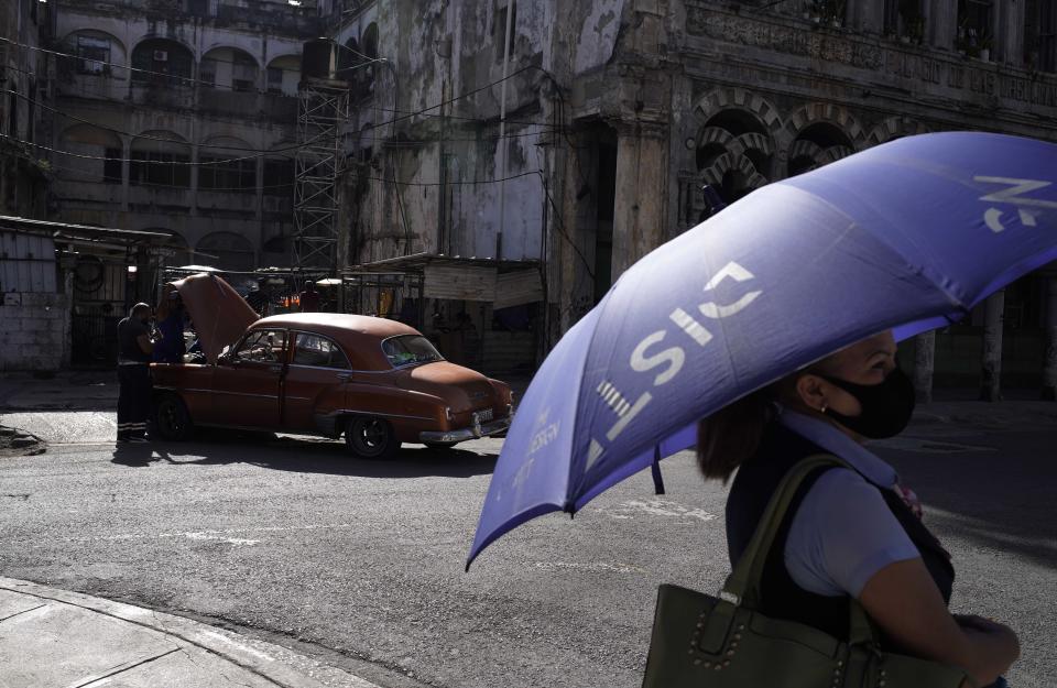 A woman stands near an old car being worked on in Old Havana, Cuba, Monday, July 12, 2021, the day after protests against food shortages and high prices amid the coronavirus crisis. (AP Photo/Eliana Aponte)