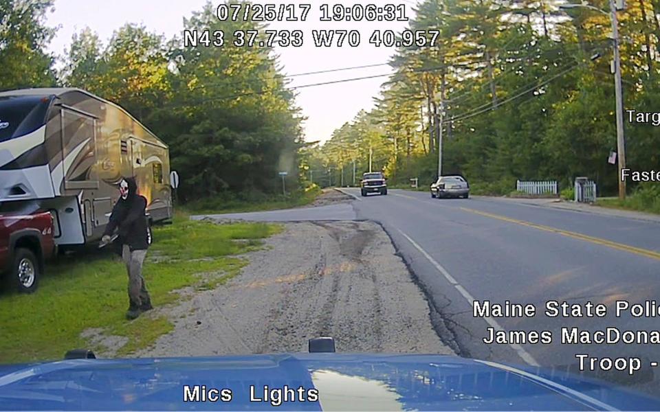 This Tuesday, July 25, 2017 patrol car dashboard camera image released by the Maine State Police shows a man strolling down a street in Hollis, Maine, who police said was wearing a clown mask with a machete taped to his amputated arm - Maine State Police