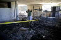 Rose-Marie Louis, a staff worker at the Orphanage of the Church of Bible Understanding, holds her head amid the charred children's home, including the unrecognizable body of a child marked by a yellow piece of paper, bottom right, in Kenscoff, on the outskirts of Port-au-Prince, Haiti, Friday, Feb. 14, 2020. A fire swept through this orphanage run by a Pennsylvania-based nonprofit group, killing over a dozen children, according to health care workers. (AP Photo/Dieu Nalio Chery)