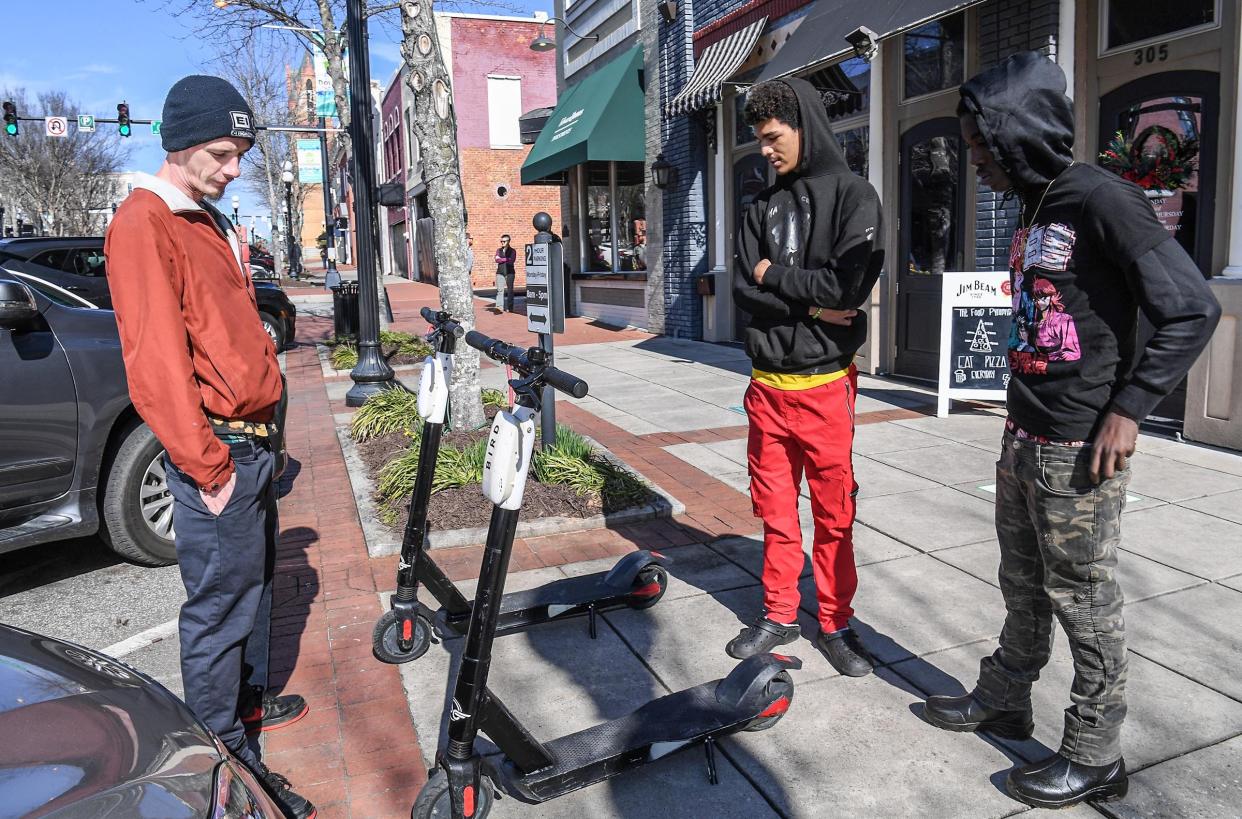 Tyler Moore, left, Bubba Thornton, and Dee Pickens look at  Bird scooters in downtown Anderson, S.C. Wednesday, January 26, 2022.