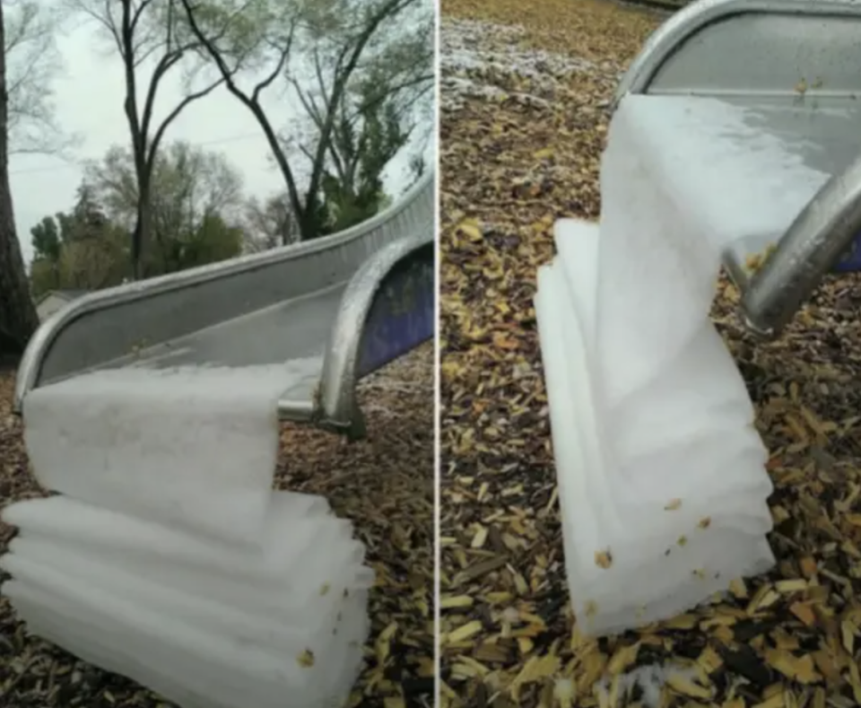 Slide covered in ice with patterns resembling draped fabric, surrounded by wood chips and trees in background