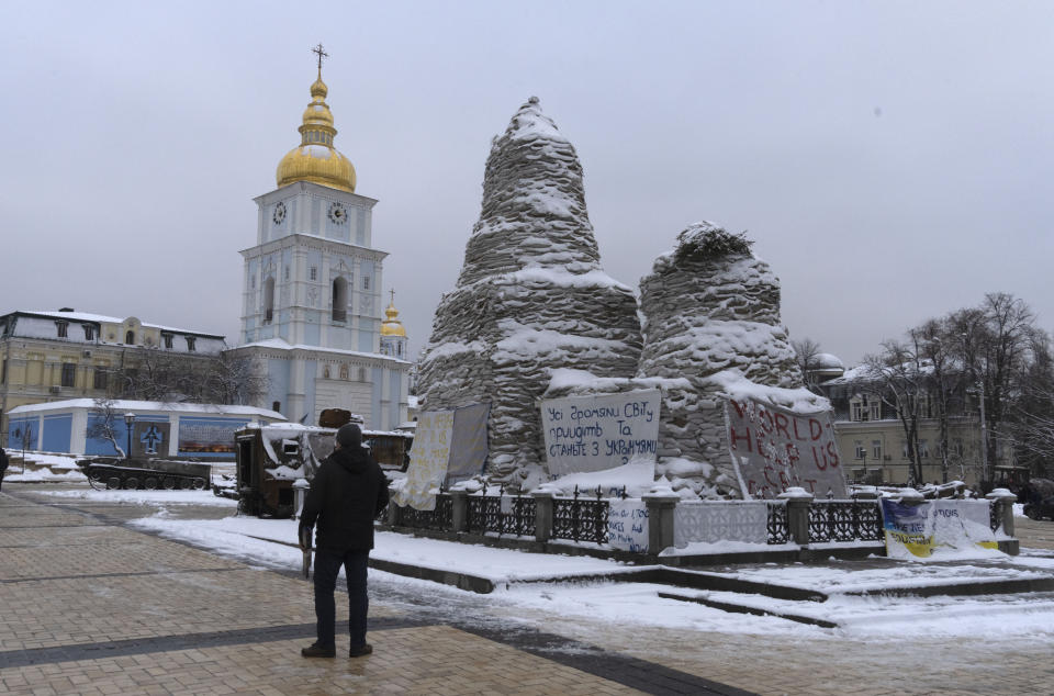 A man looks at St. Michael Cathedral standing near a monument to Princess Olga covered with sand bags to protect it from the Russian shelling, with placards displayed near the monument calling to support Ukraine, in central Kyiv, Ukraine, Monday, Dec. 12, 2022. Ukraine has been fighting with the Russian invaders since Feb. 24 for over nine months. (AP Photo/Efrem Lukatsky)