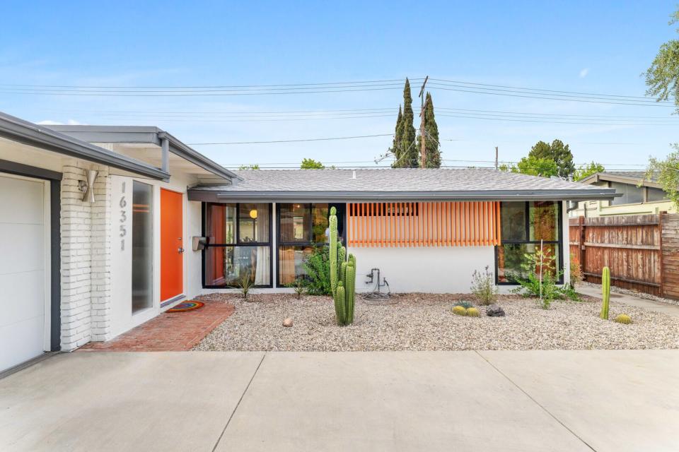 A bright orange front door pops against the crisp white exterior and native landscaping.