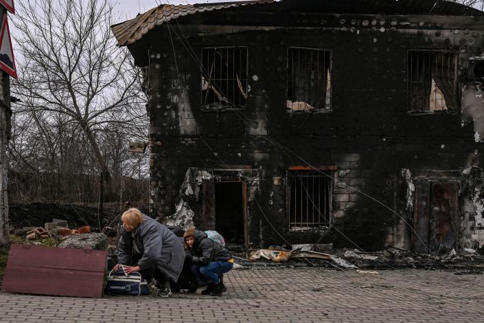 bucha ukraine two people with luggage crouch behind a boulder in front of a burnt blackened building