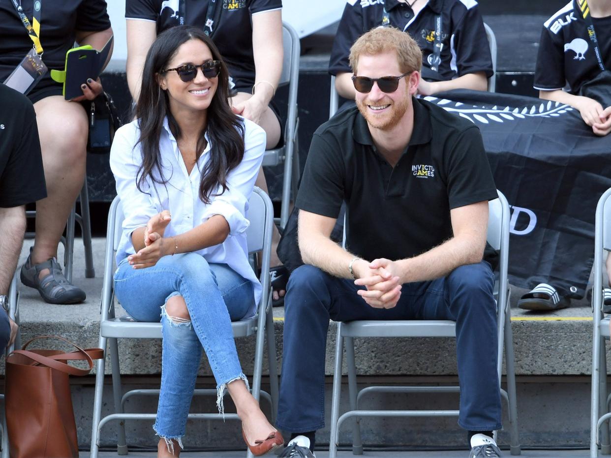 Meghan Markle and Prince Harry laugh as they sit in folding chairs.