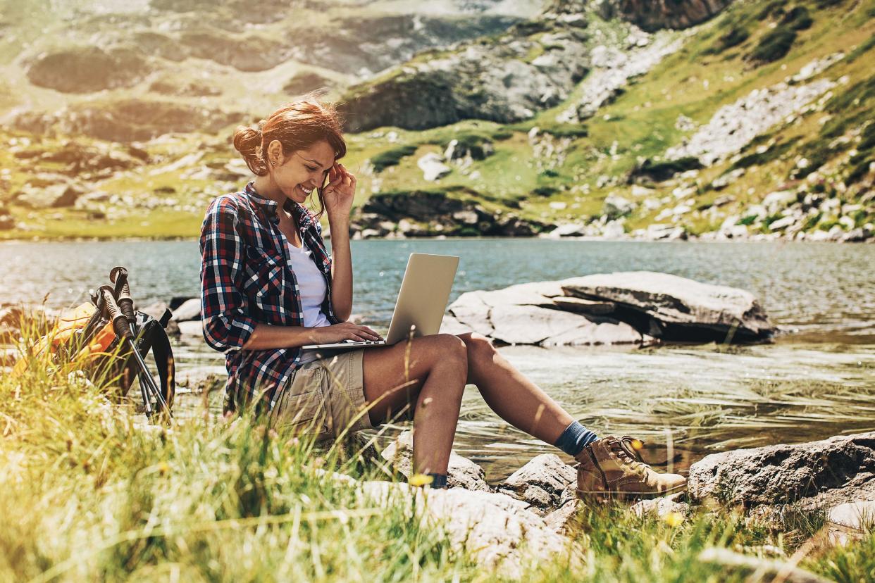 woman with laptop, sitting on rock in national park